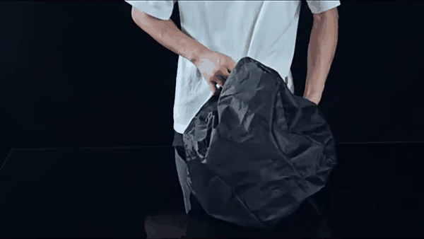 Deux mains passent la housse de pluie par-dessus le sac, qui se retrouve entièrement couvert